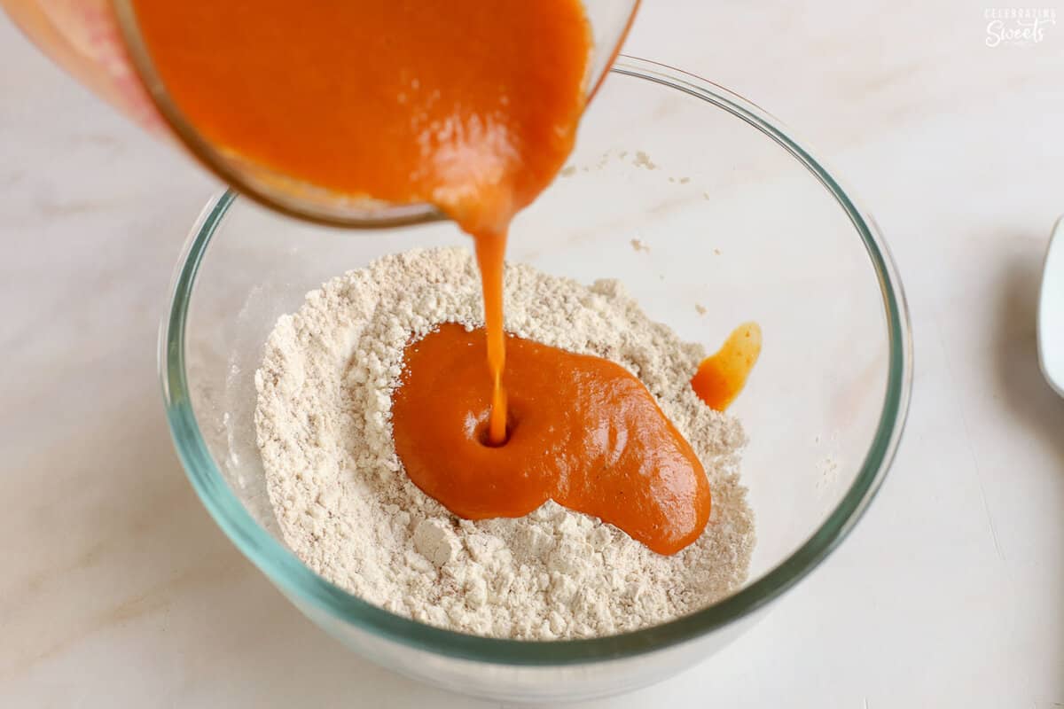Pumpkin puree being poured into flour in a glass bowl.