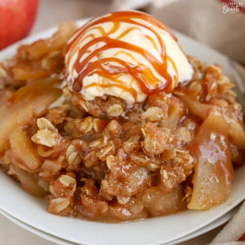Apple crisp on a white plate topped with vanilla ice cream and caramel sauce.