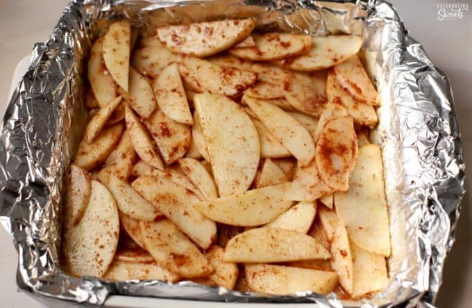 Unbaked cinnamon apple slices in a foil-lined square baking pan.