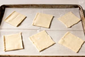 Six squares of puff pastry on a parchment lined baking sheet.