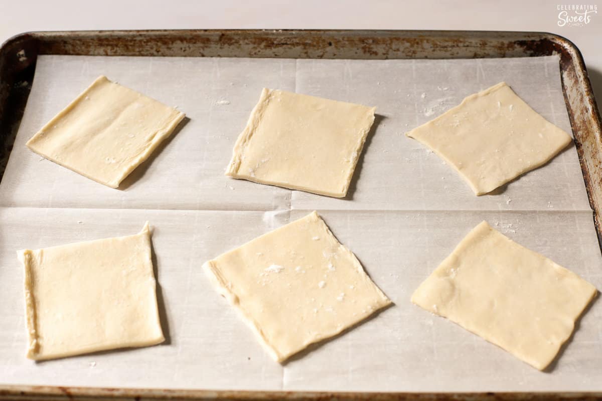 Six squares of puff pastry on a parchment lined baking sheet.