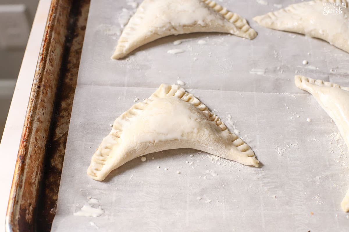 Unbaked apple turnovers on a parchment lined baking sheet.