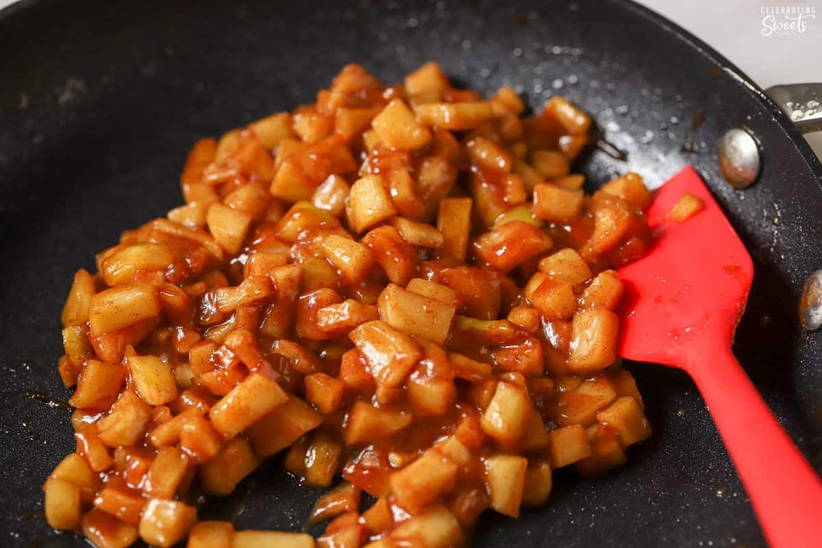 Diced cinnamon apples in a black pan with a red spatula.