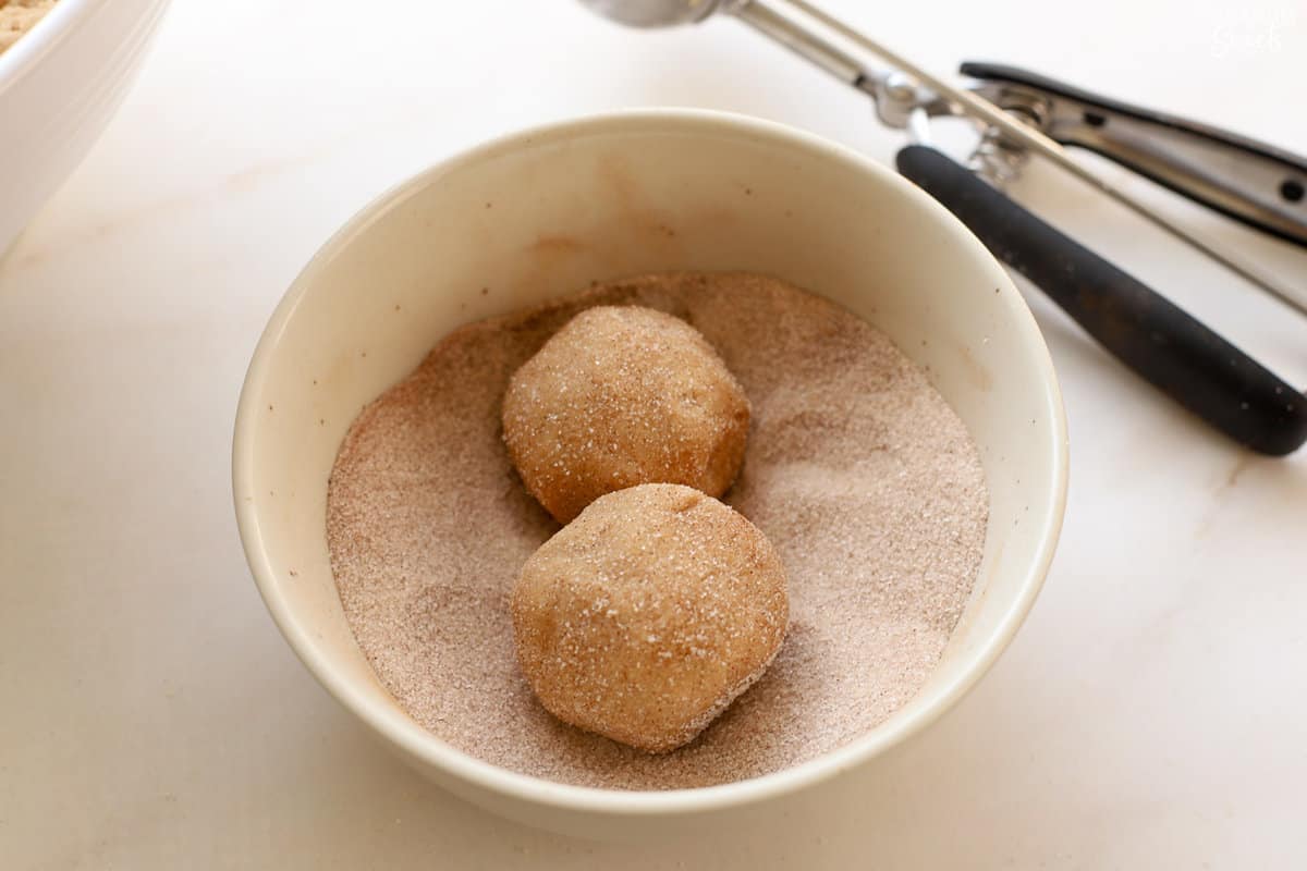 Cookie dough balls in a bowl of cinnamon sugar.