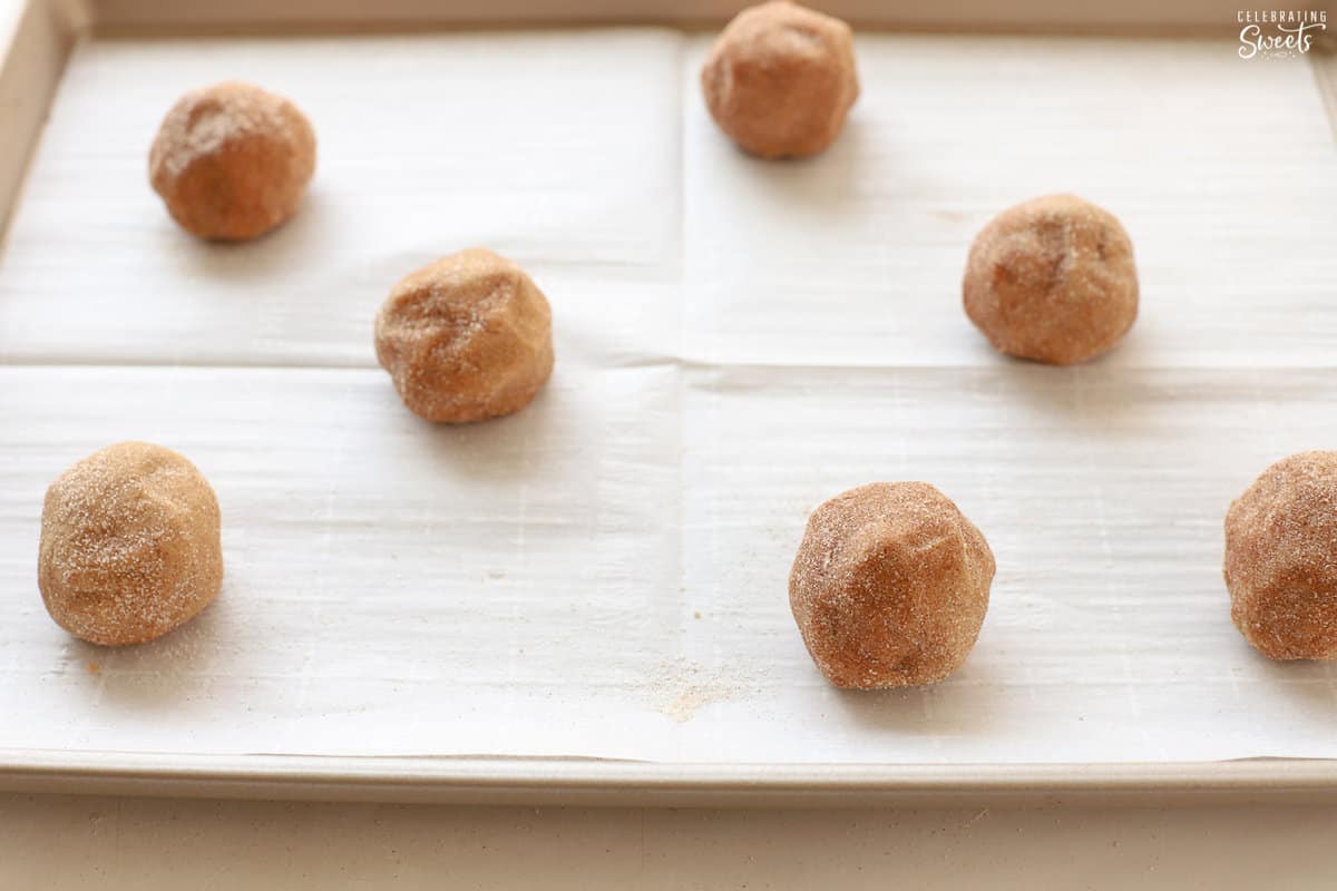 Seven cookie dough balls on a parchment-lined baking sheet.
