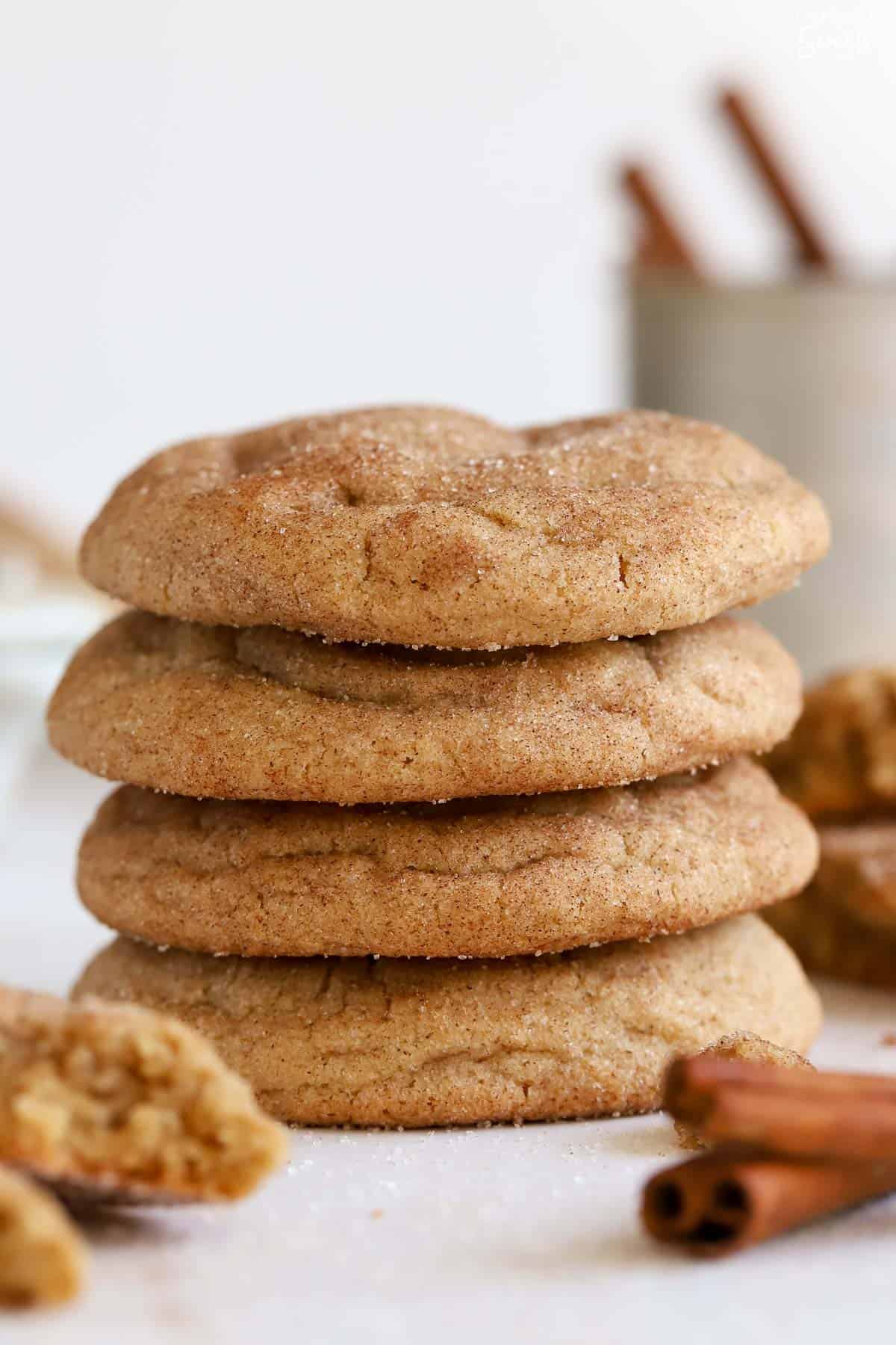 Stack of four maple snickerdoodle cookies with cinnamon sticks in the background.