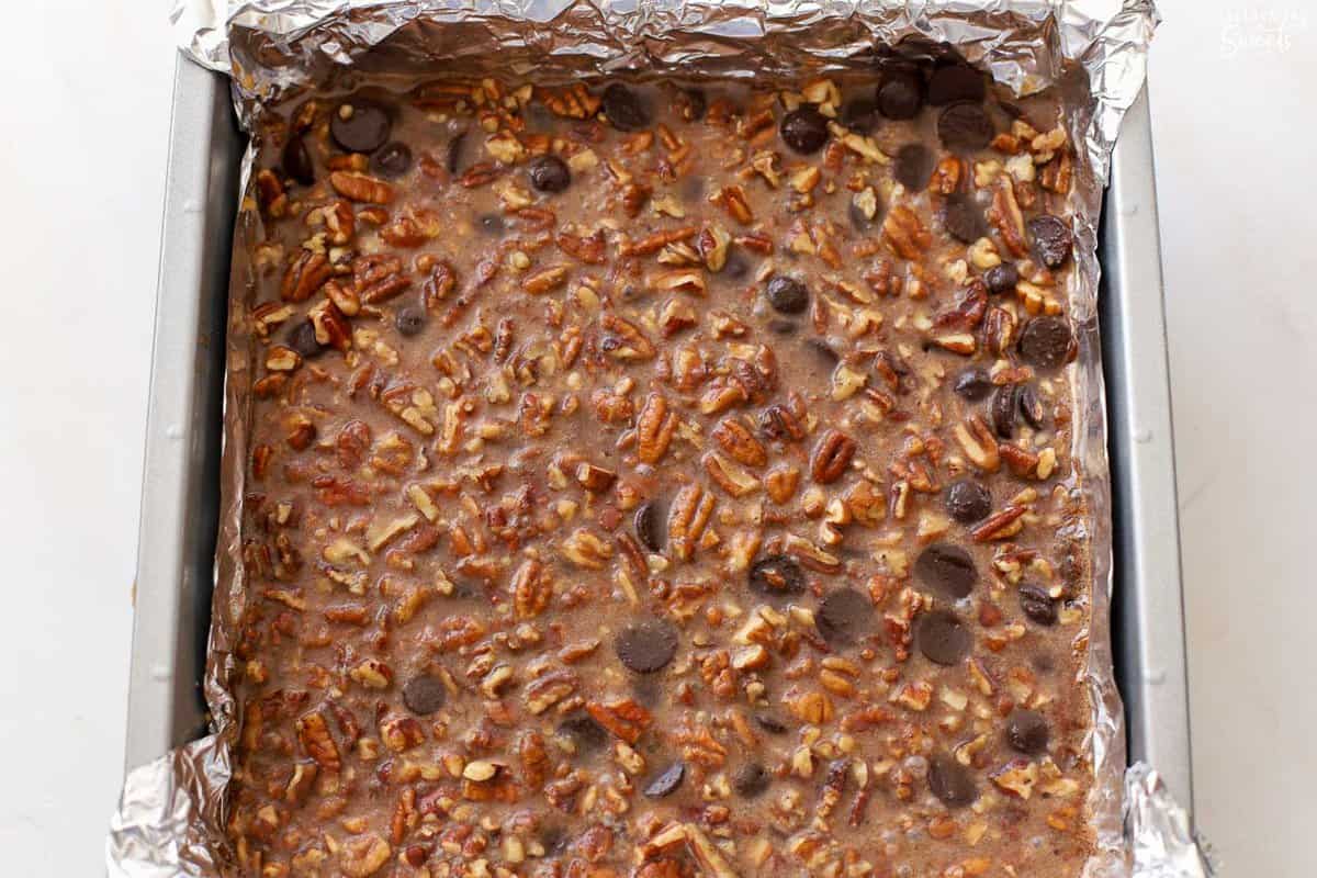 Unbaked chocolate pecan bars in a foil lined baking dish.
