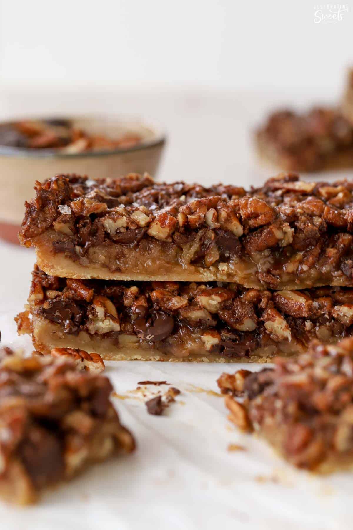 Stack of chocolate pecan bars on white parchment paper.