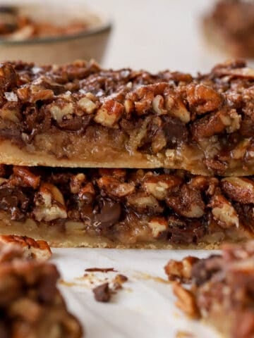 Stack of chocolate pecan bars on white parchment paper.