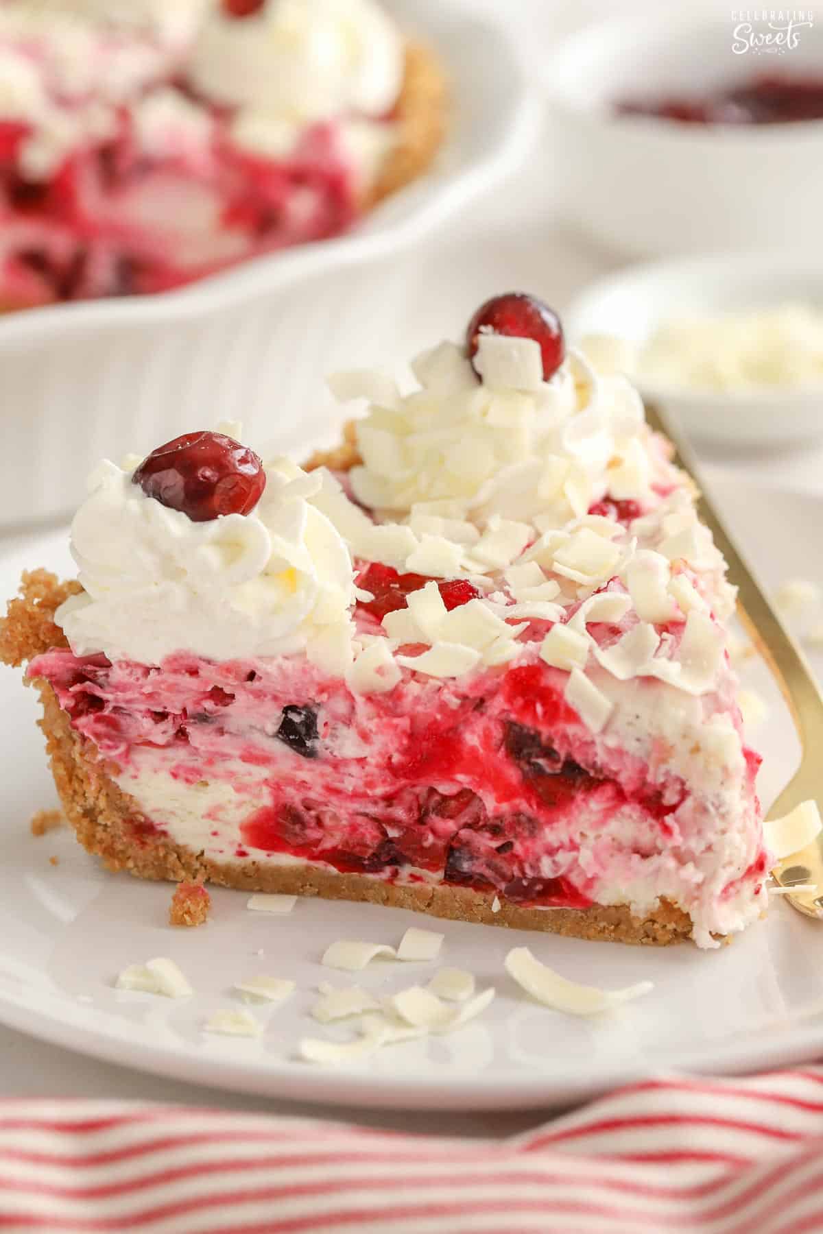 Slice of cranberry cheesecake topped with whipped cream and white chocolate shavings. 