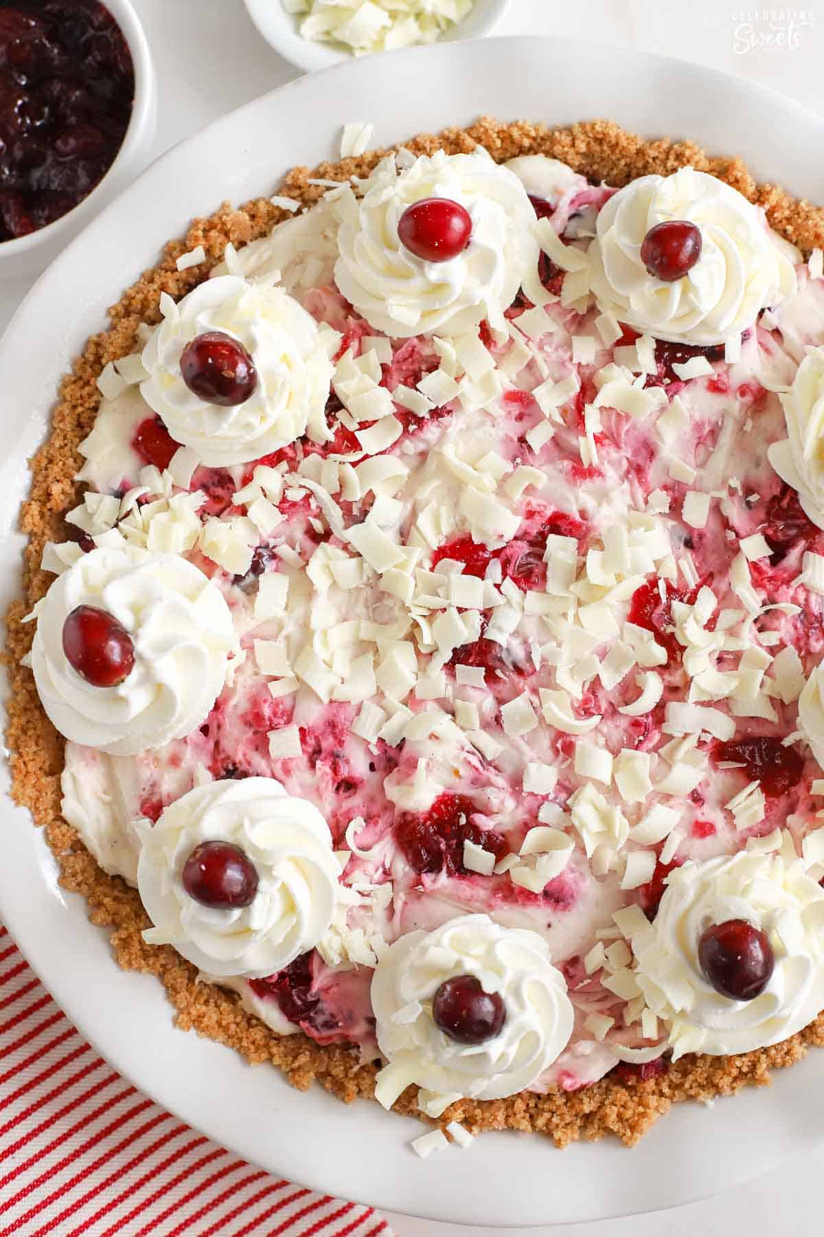 White chocolate cranberry cheesecake decorated with white chocolate shavings, whipped cream, and fresh cranberries.