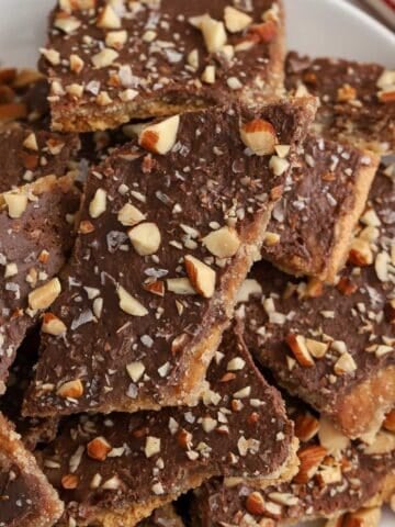 Graham cracker toffee topped with chopped almonds on a white plate next to a red and white striped napkin.