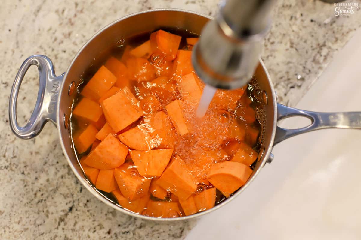 Water being poured over sweet potato chunks in a saucepan.