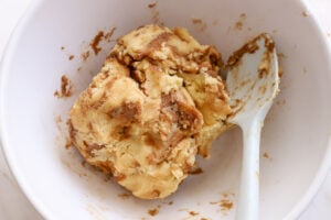 Cinnamon roll cookie dough in a white bowl with a rubber spatula.