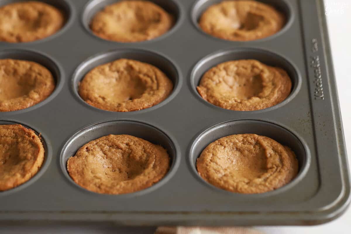 Gingerbread cookie cups in a muffin pan.