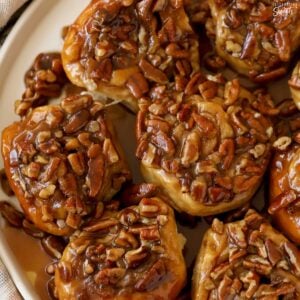 Sticky buns topped with pecans on a white plate.