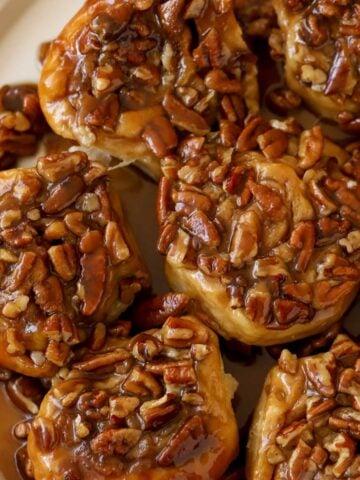 Sticky buns topped with pecans on a white plate.