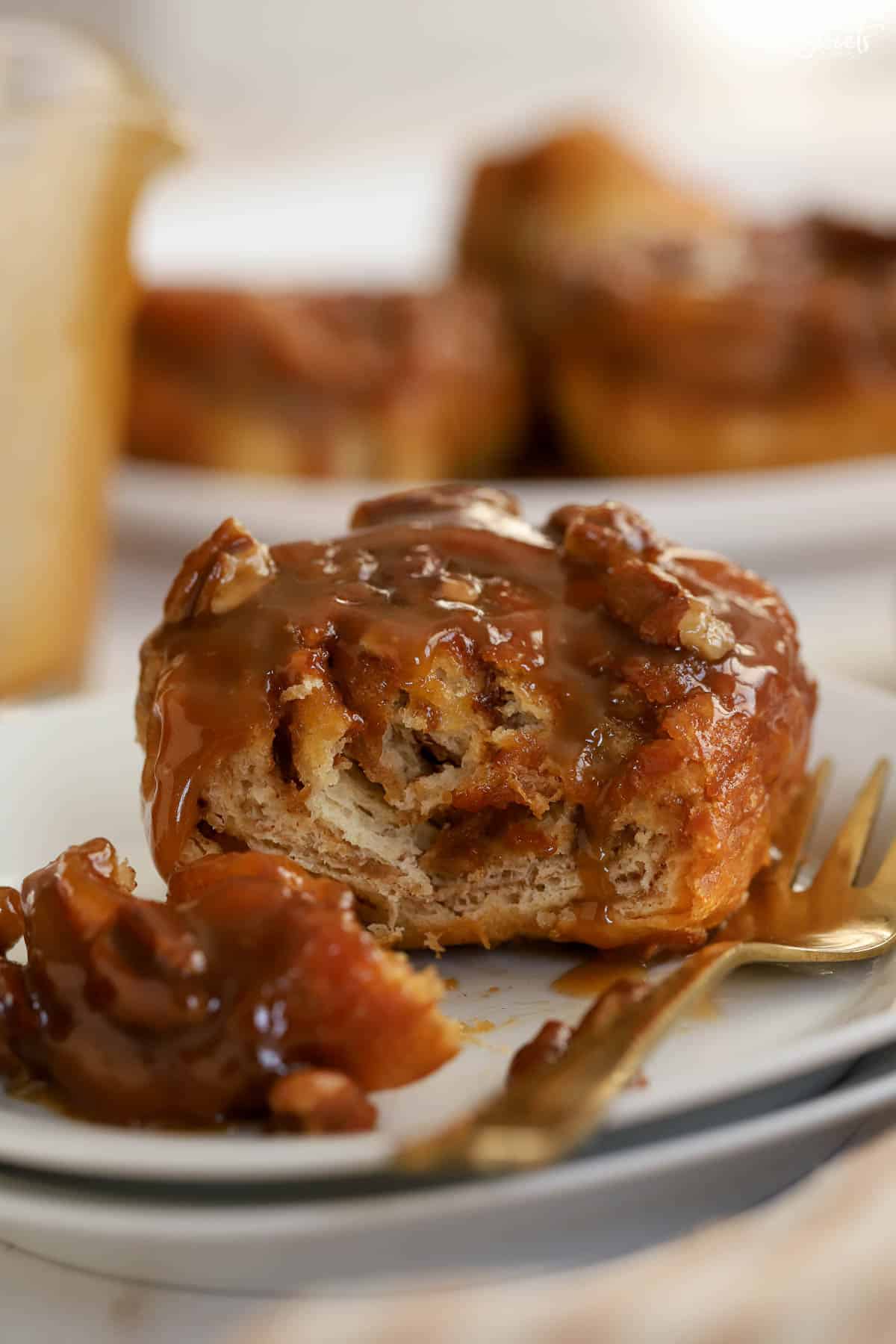 Sticky bun cut open on a white plate with a gold fork.