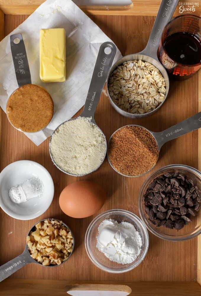 Ingredients for making healthy chocolate chip cookies (nuts, chocolate, egg, almonds, sugar, oats, butter, syrup).