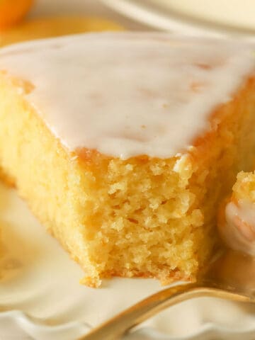 Slice of lemon olive oil cake on a white plate with a gold fork.