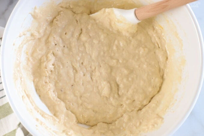 Pancake batter in a white bowl with a wooden spatula.