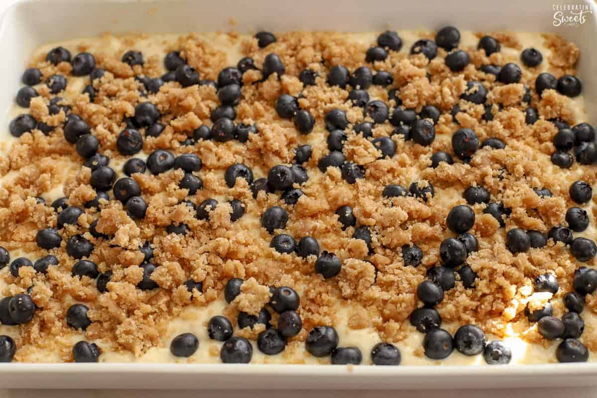 Blueberries and crumb topping on top of pancake batter in a white dish.