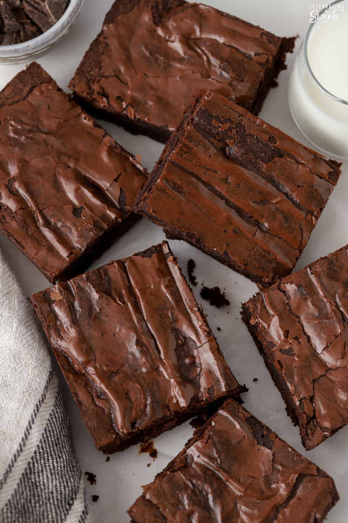 Squares of brownies next to a towel tea towel and a glass of milk.