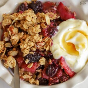 Berry crisp in a white bowl with a scoop of yogurt.