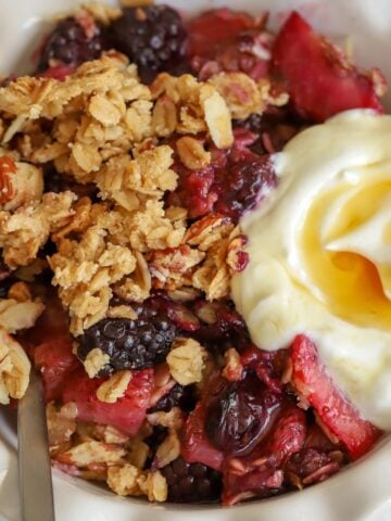 Berry crisp in a white bowl with a scoop of yogurt.