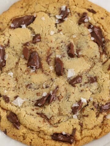 Closeup of a large chocolate chip cookie on a parchment lined baking sheet.