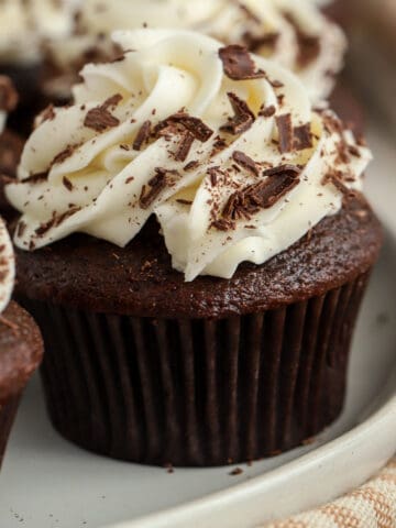 Chocolate cupcake topped with white frosting and chocolate shavings.