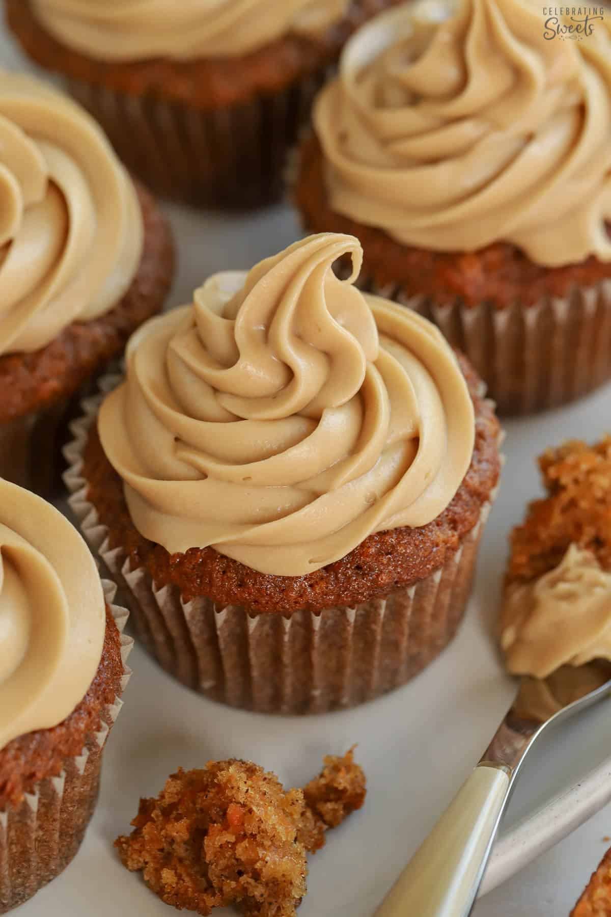 Carrot cake cupcake topped with swirled brown sugar frosting on a grey plate next to a fork.