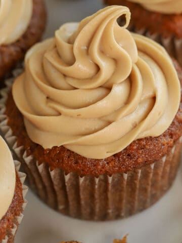 Carrot cake cupcake topped with swirled brown sugar frosting on a grey plate.