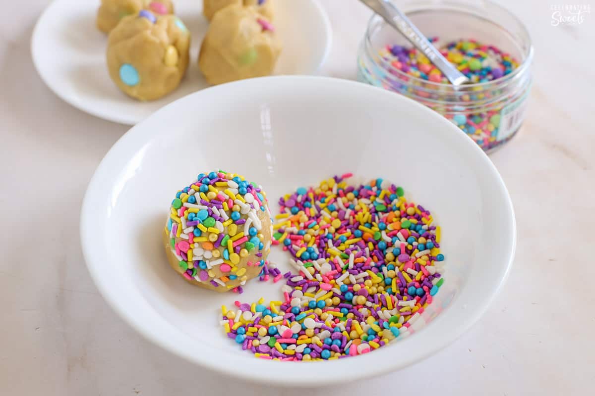 Cookie dough ball in a bowl of pastel sprinkles.
