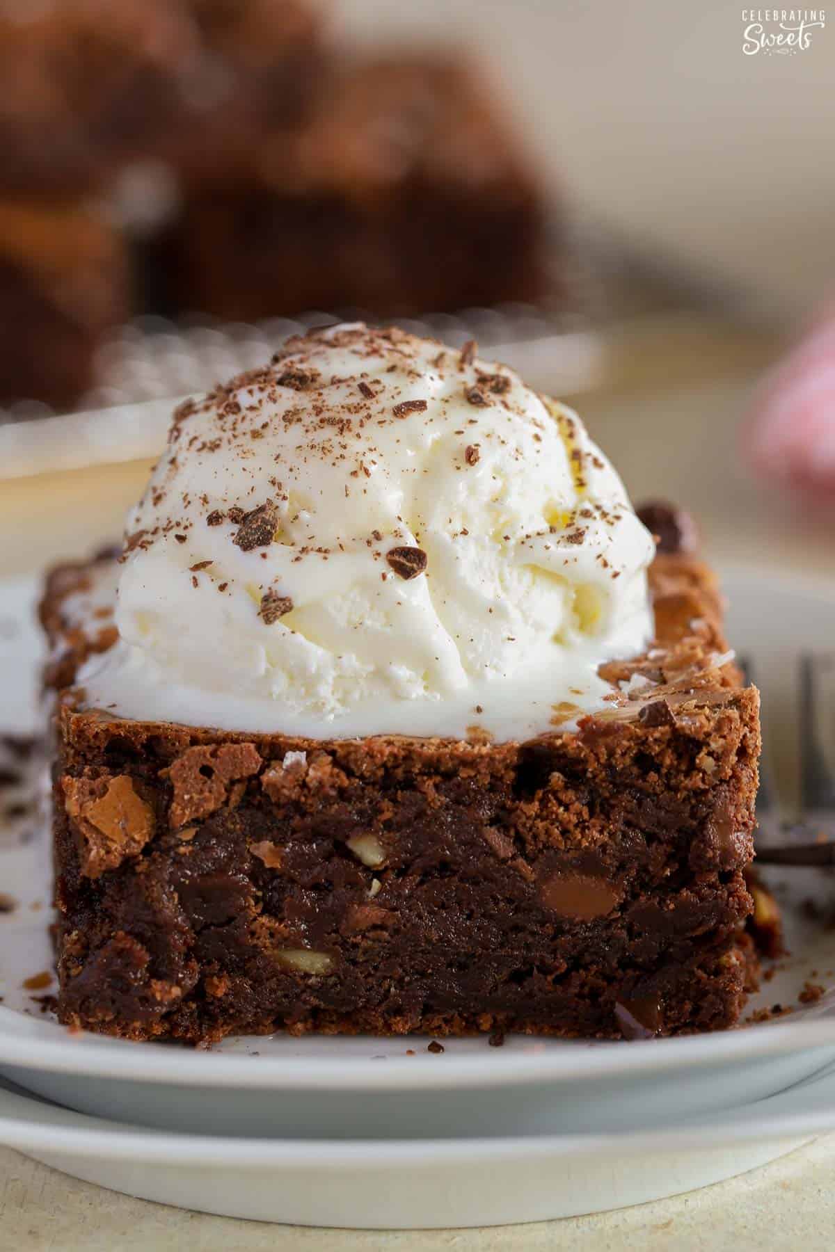 Closeup of a homemade brownie topped with ice cream on a white plate.