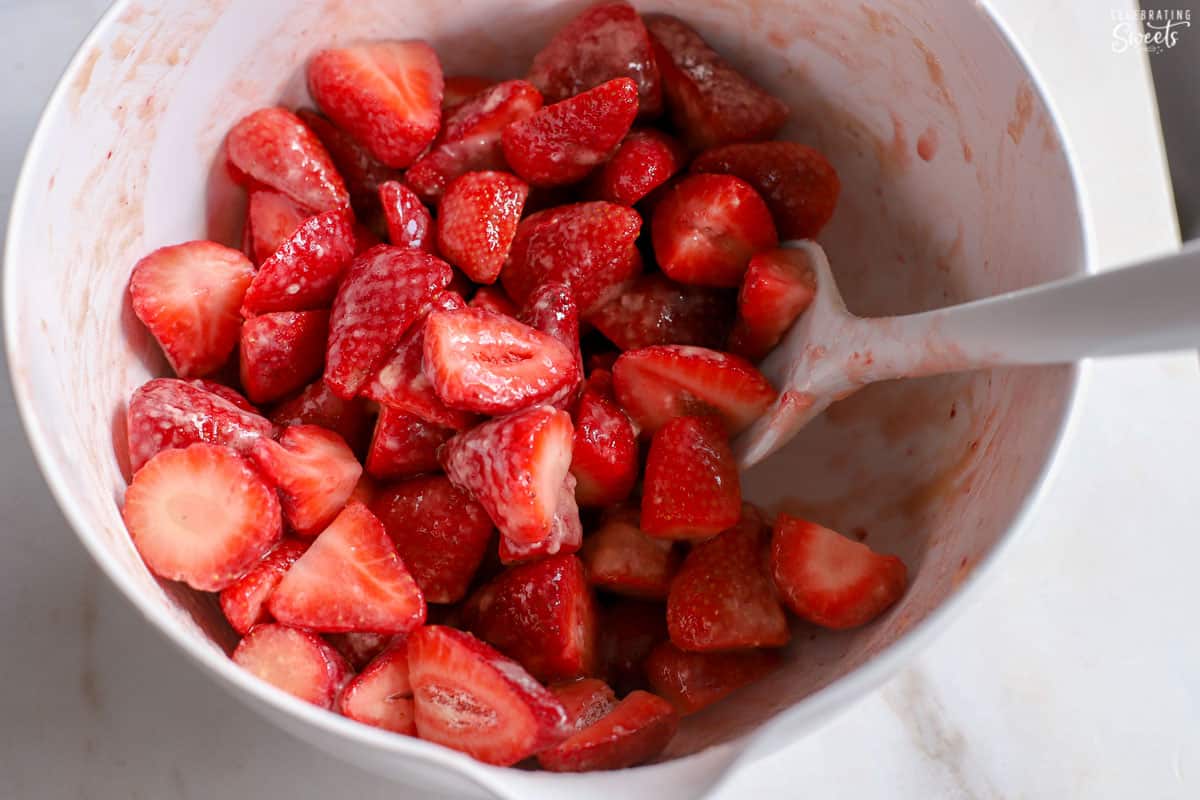 Strawberries and a rubber spatula in a white bowl.