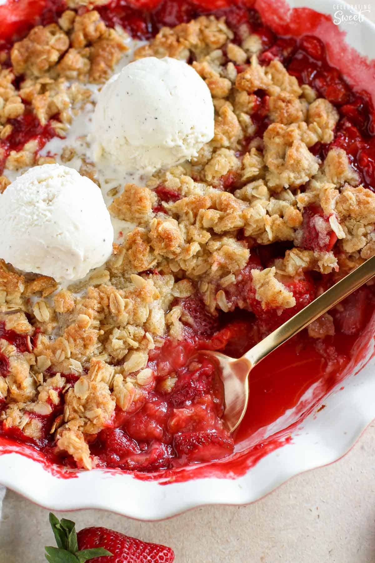 Strawberry crisp in a white baking dish topped with two scoops of vanilla ice cream.