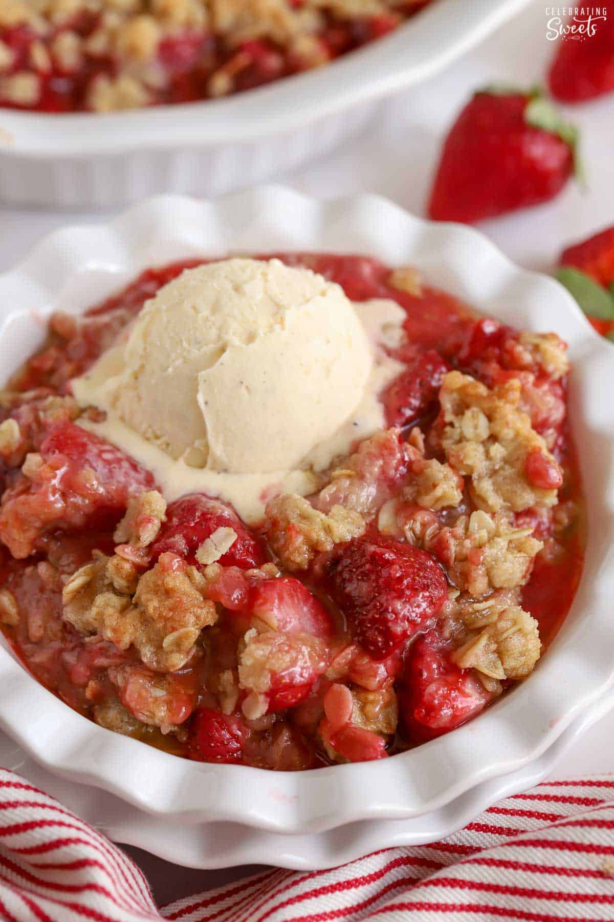 Strawberry crisp in a white bowl topped with ice cream.
