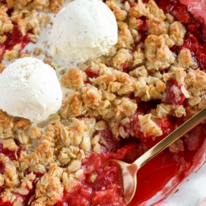 Strawberry crisp in a white baking dish topped with two scoops of vanilla ice cream.