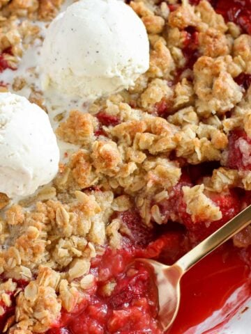 Strawberry crisp in a white baking dish topped with two scoops of vanilla ice cream.