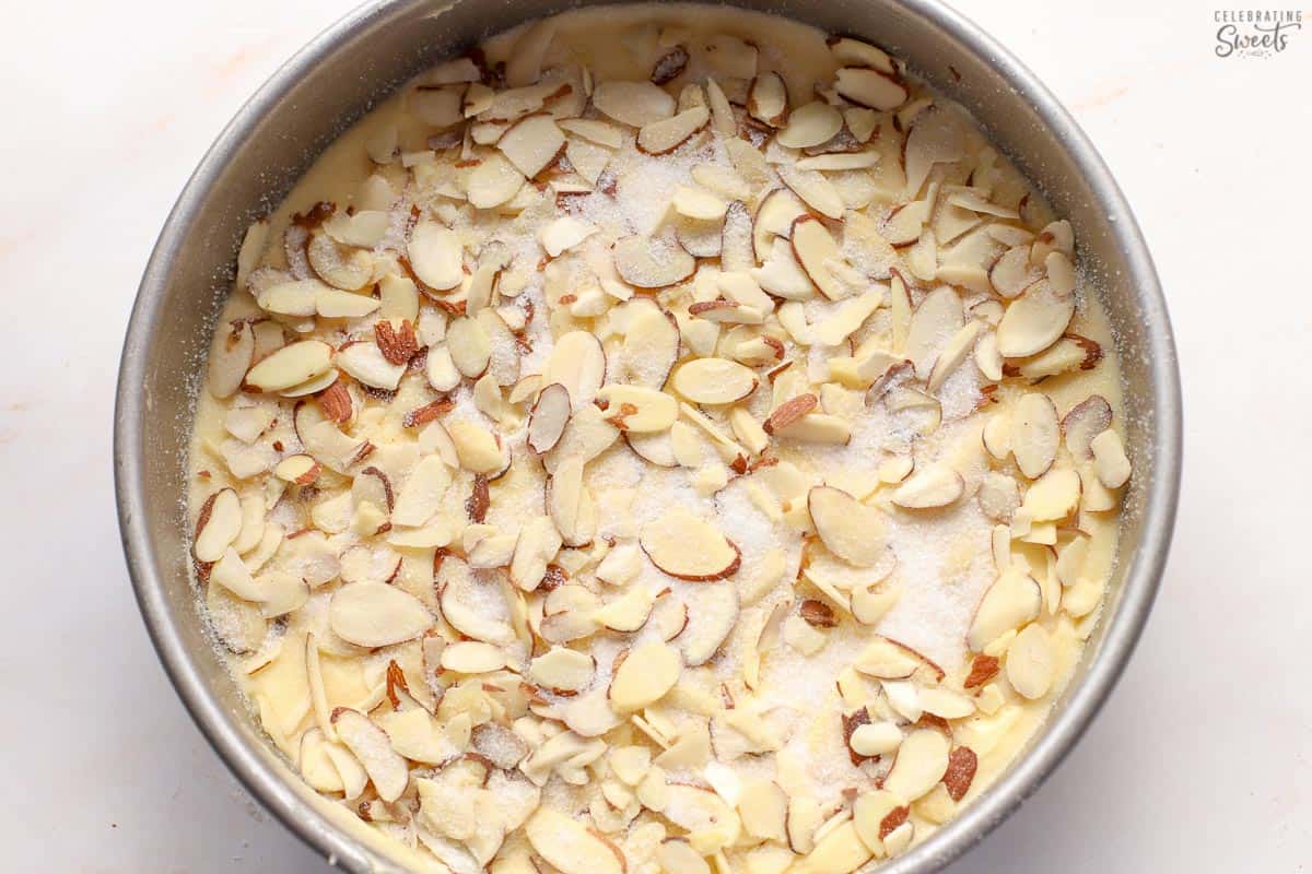 Almond cake topped with sliced almonds and sugar in a round cake pan.