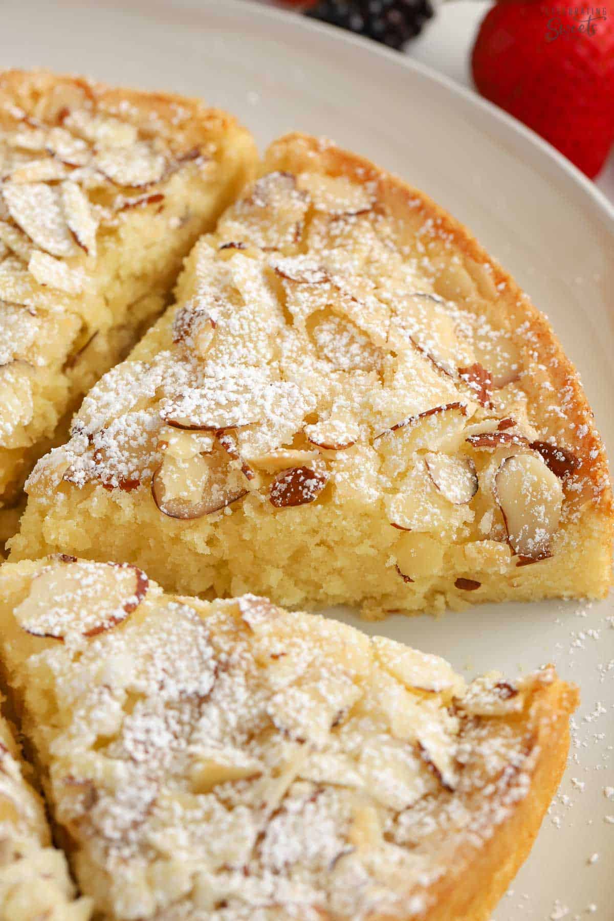 Slice of almond cake topped with sliced almonds and powdered sugar.
