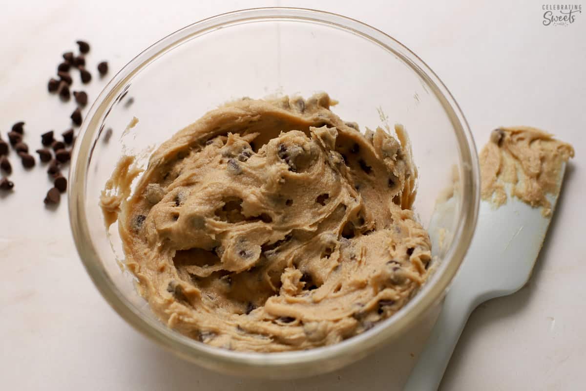 Cookie dough in a glass bowl next to a grey spatula.