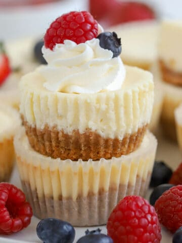 Two mini cheesecakes stacked on top of each other topped with berries and whipped cream.