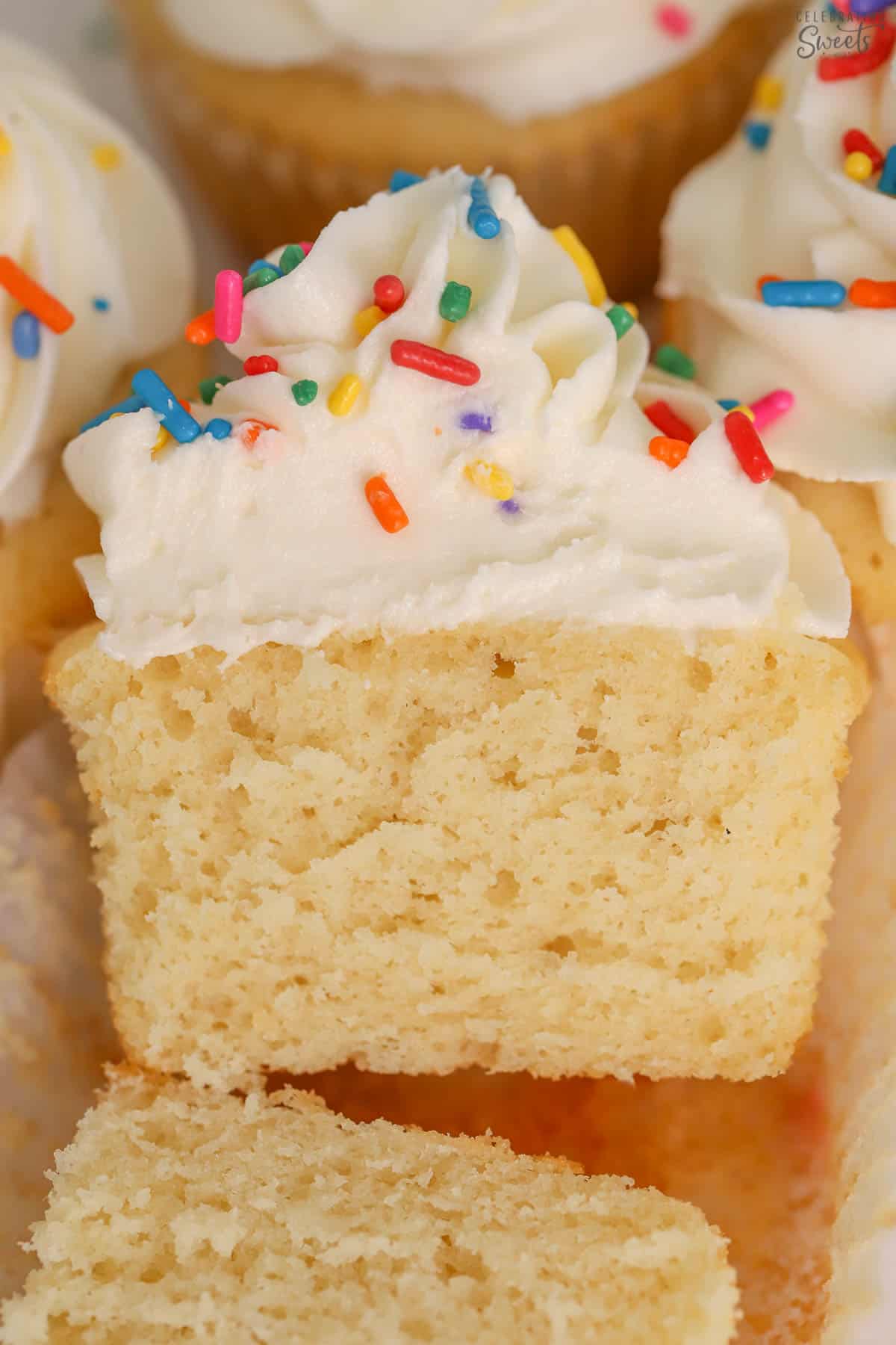 Vanilla cupcake topped with white frosting and sprinkles cut in half.