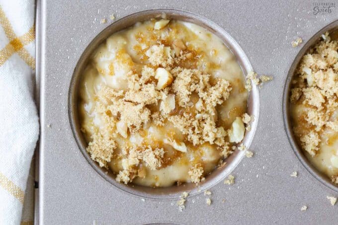 Unbaked banana nut muffin batter in a muffin pan topped with brown sugar and chopped nuts.