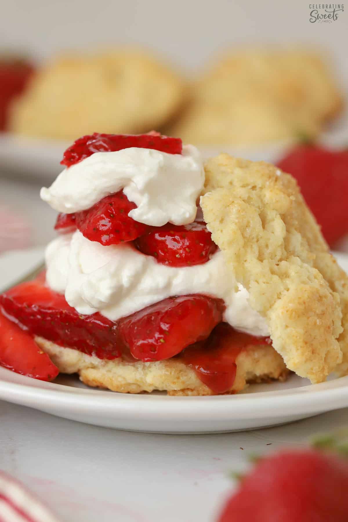 Layered strawberry shortcake on a white plate next to a fresh strawberry.