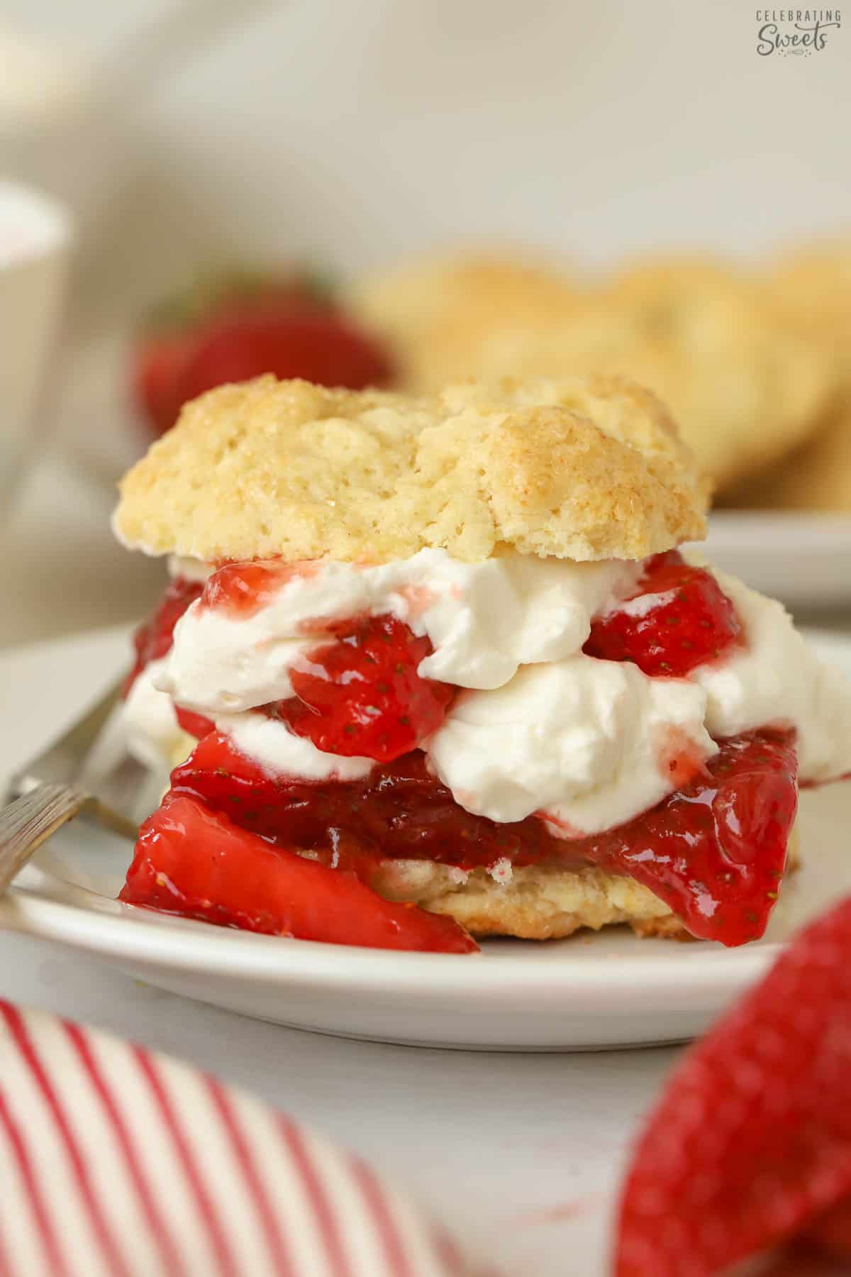 Layered strawberry shortcake on a white plate next to a fresh strawberry.