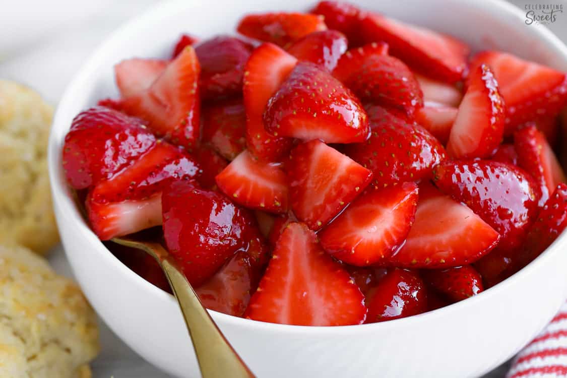 Strawberries in a white bowl with a gold spoon.