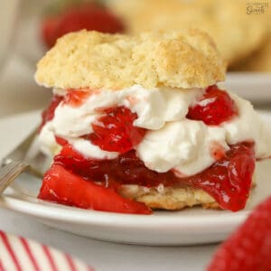 Layered strawberry shortcake on a white plate next to a fresh strawberry.